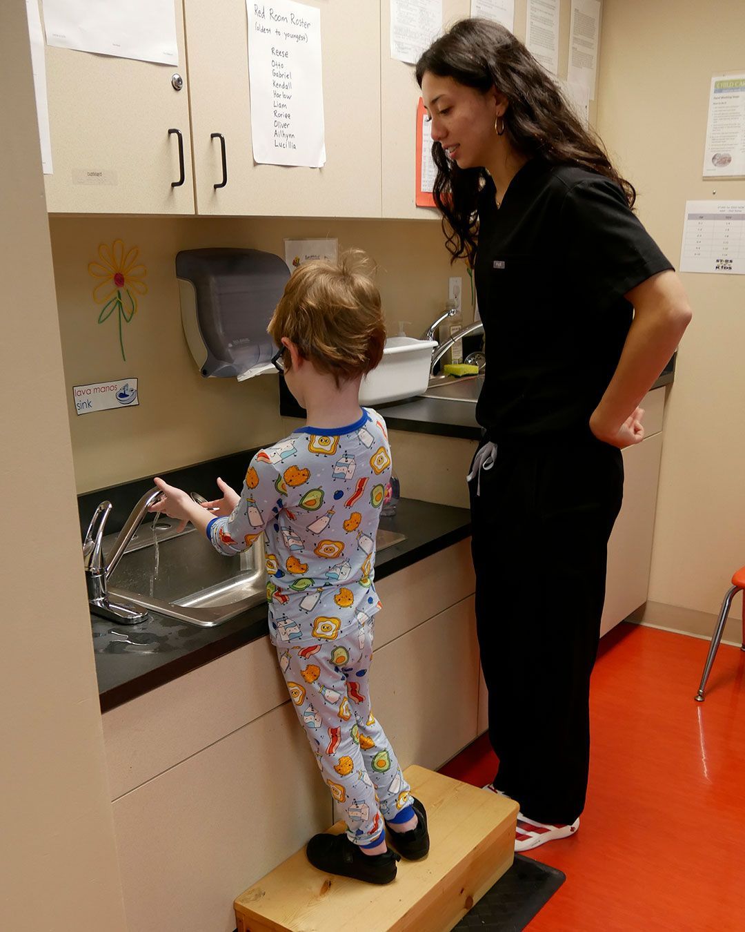 A small boy washes his hands while a female physician assistant student watches.