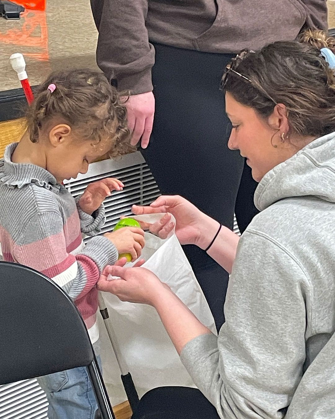 A volunteer helps a small girl place her Easter egg in her bag.