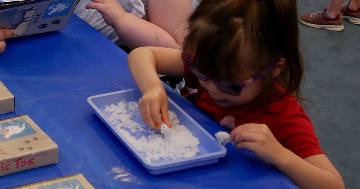 A small girl plays with a tray of Insta Snow.