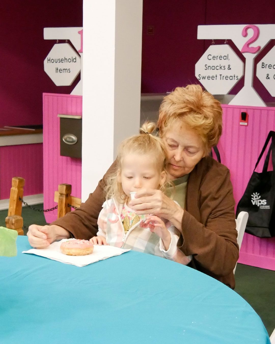 A grandmother helps her granddaughter with a glass of juice and a donut with sprinkles.