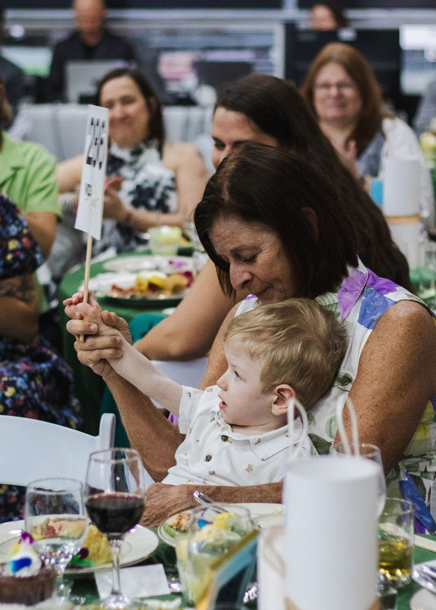 A woman and a small boy, seated in her lap, both raise and auction paddle to bo bid during the Gala auction.