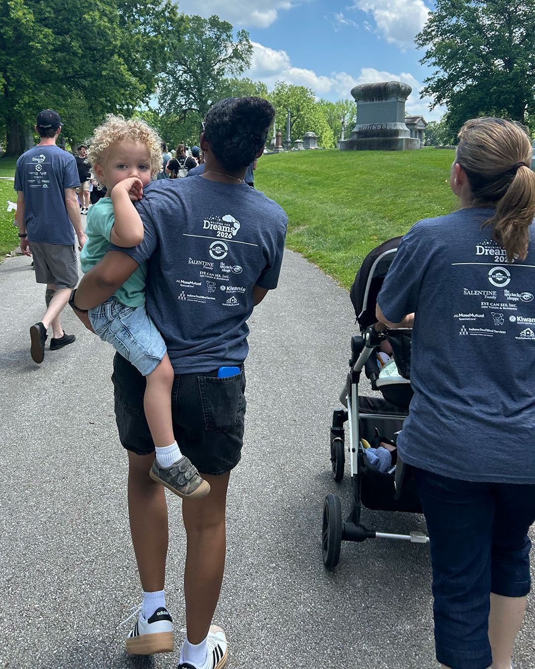 A mother carrying her daughter on her hip and another pushing a stroller during Walking for Dreams.