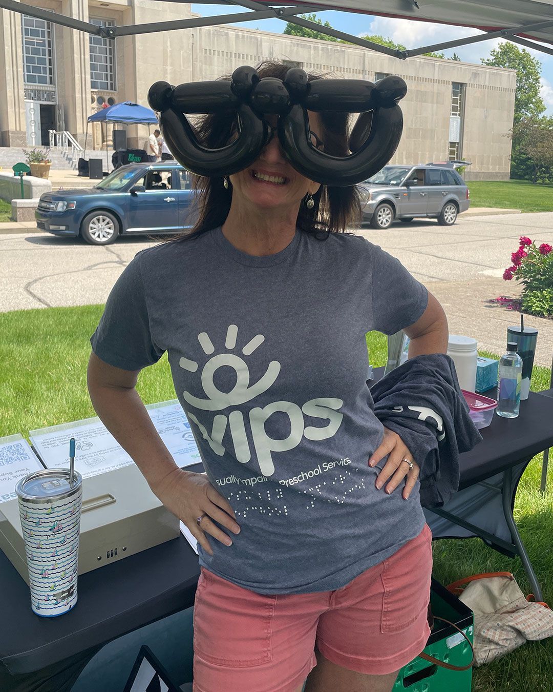 Sheila poses for a photo behind the registration table while wearing glasses made from balloons during Walking for Dreams,