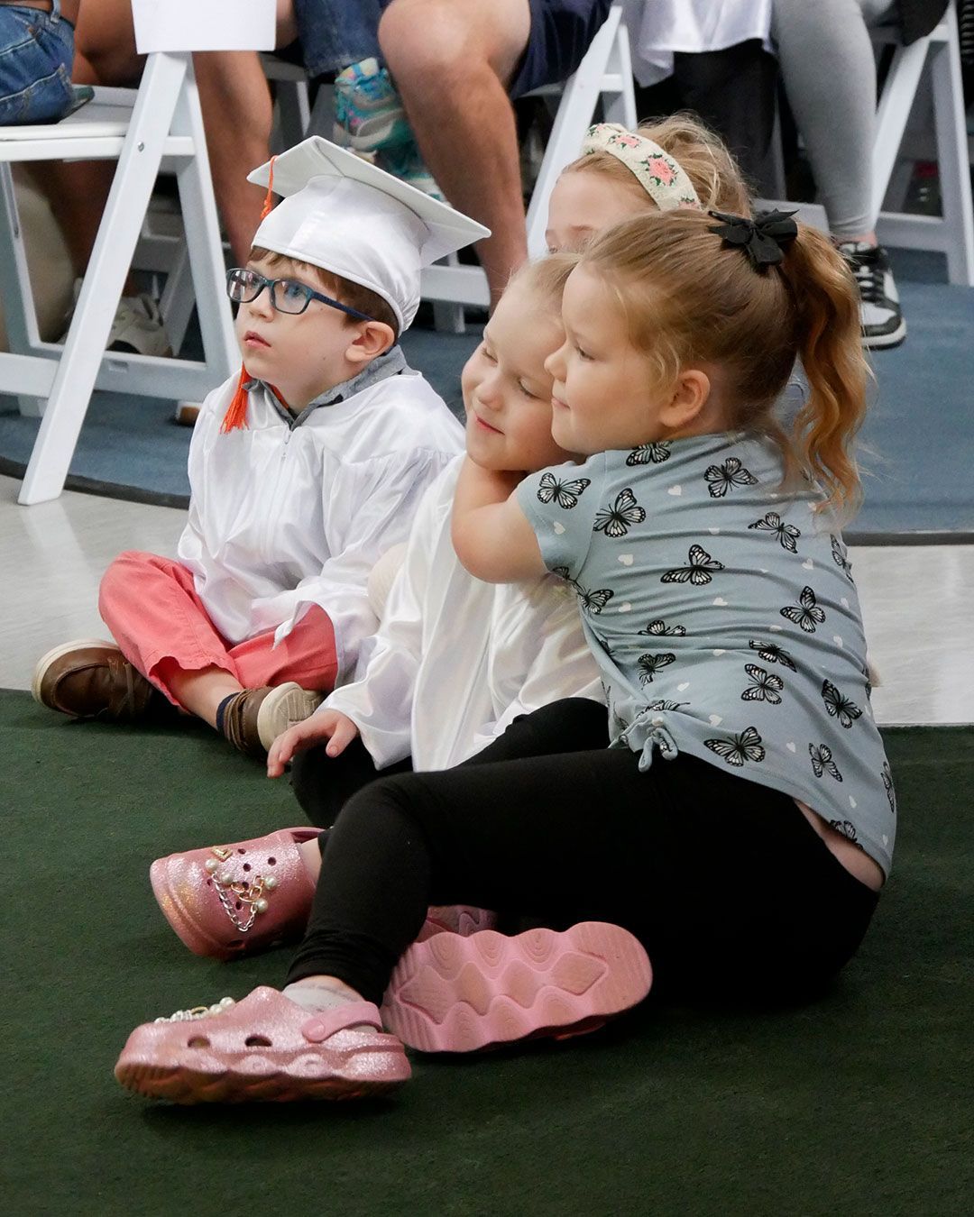 Children sit on the floor and watch the graduation presentation.