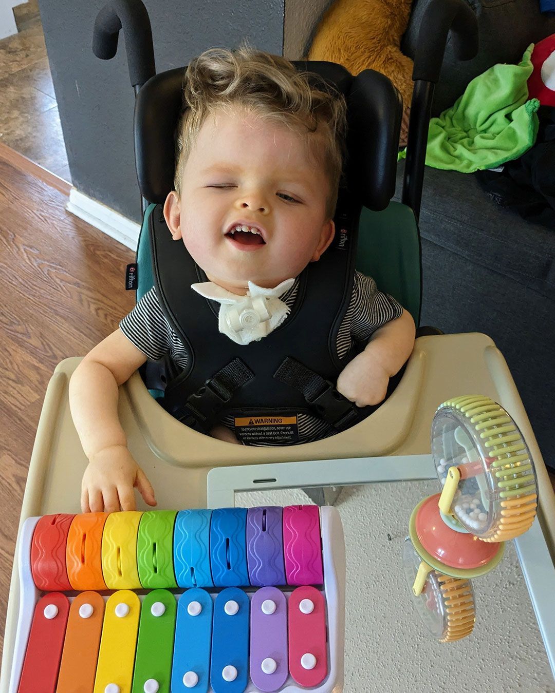 Sonny sits in chair, smiling and playing with an interactive toy.