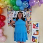 Woman standing in front of colorful balloons and a VIPS sign, smiles for the camera.