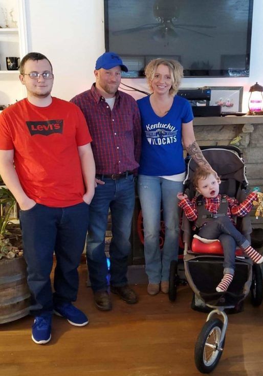 A family stands up with their child in an adaptive stroller near by.