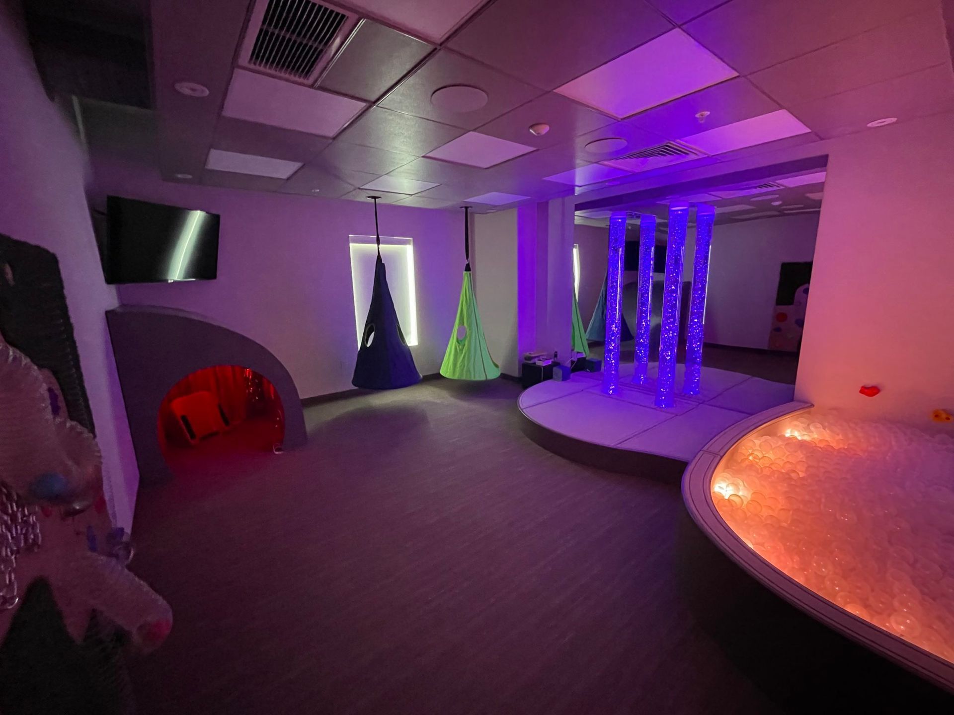 Darker room with light up ball pit, light up bubble tubes, and swings.