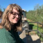 Woman with glasses outside with a small smile on her face.