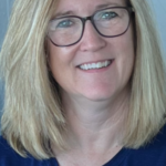Woman with glasses and blonde hair smiling.