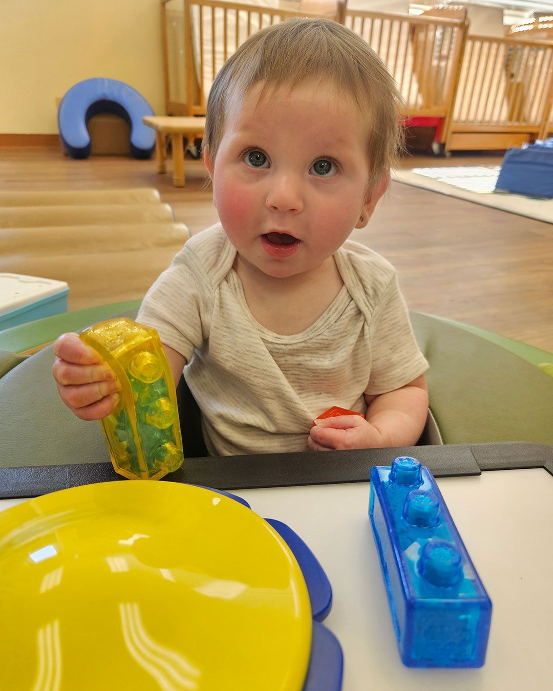 Eleanor is holding her building blocks and reacting to someone off camera.