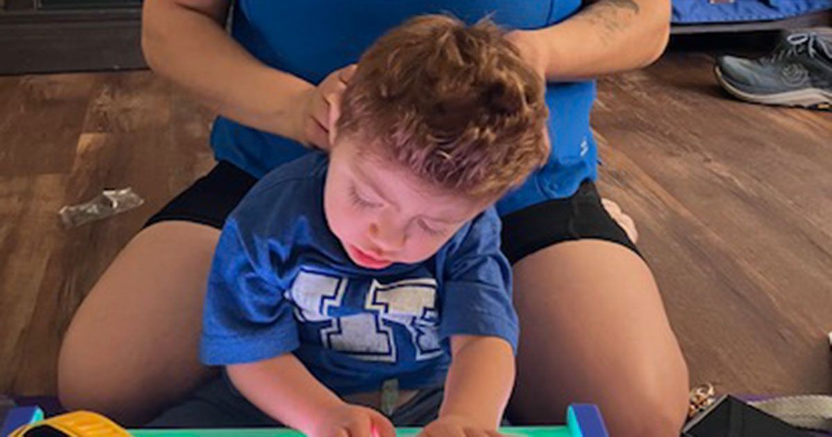 Harvey is using a switch-activated car while his mother sits behind him.