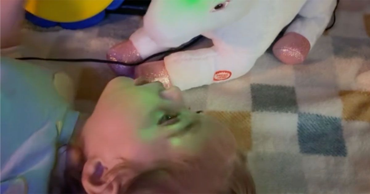 Adaline is lying on a blanket, interacting with her unicorn toy that lights up and plays music.