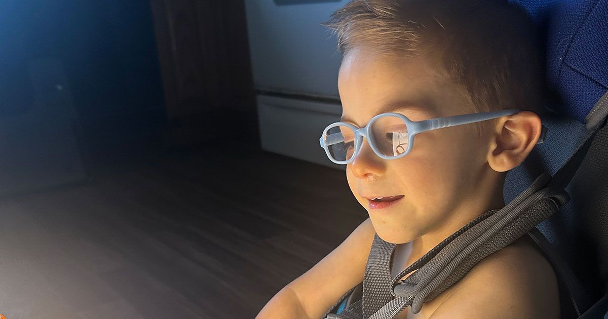 Elliot is smiling while wearing his glasses and interacting with his light box.