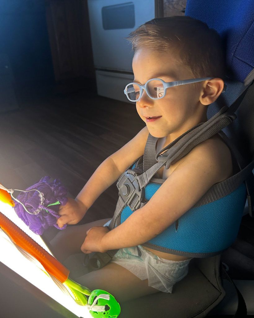 Elliot is smiling while wearing his glasses and interacting with his light box.