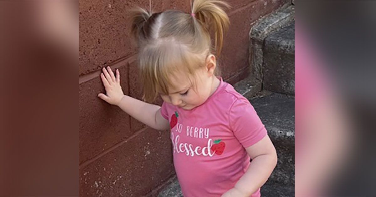 Emery is walking down concrete stairs, steadying herself with her hand on the wall.