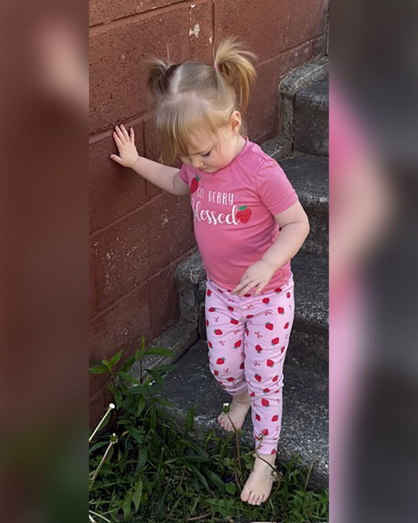 Emery is walking down concrete stairs, steadying herself with her hand on the wall.