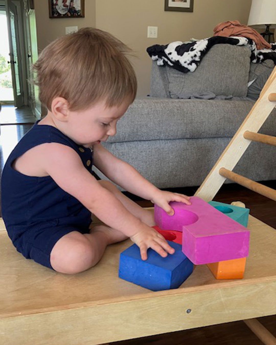 Luke is sitting and putting together large, brightly colored building blocks.