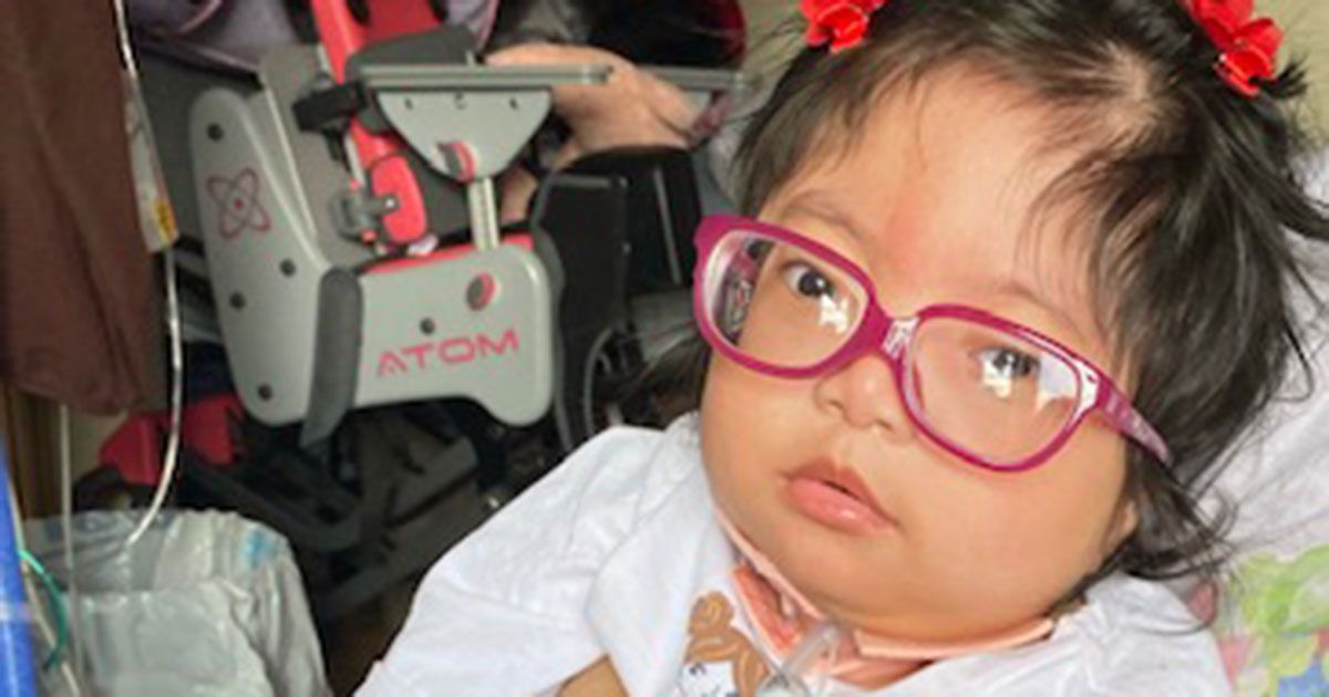 Mirielle is wearing her red glasses and sitting in her mother's lap.