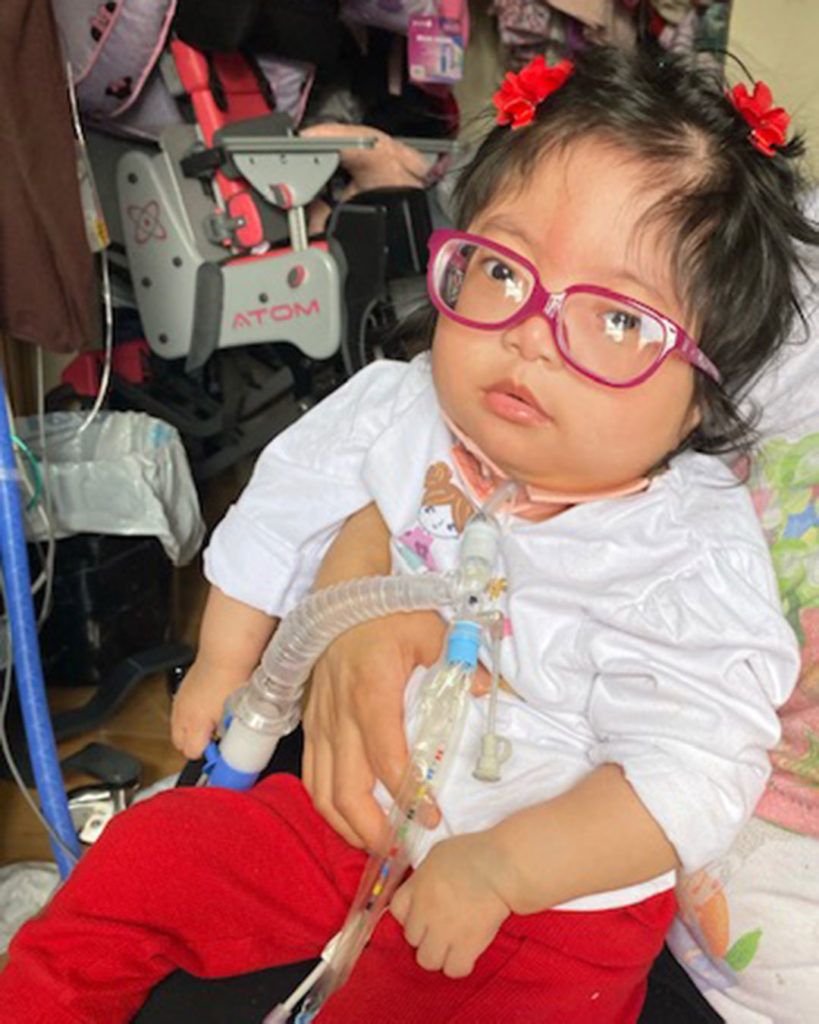 Mirielle is wearing her red glasses and sitting in her mother's lap.