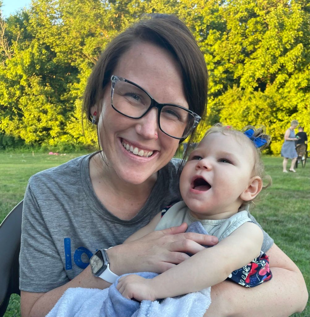 A woman with glasses smiles while holding her baby girl.