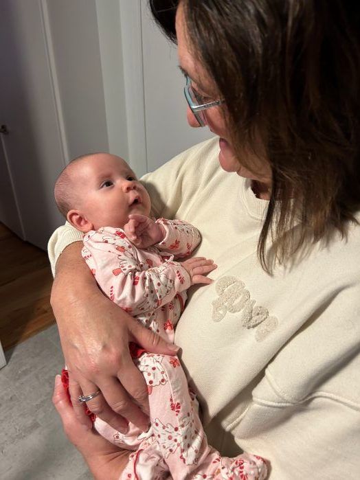 A woman holds a small baby who is looking at her.