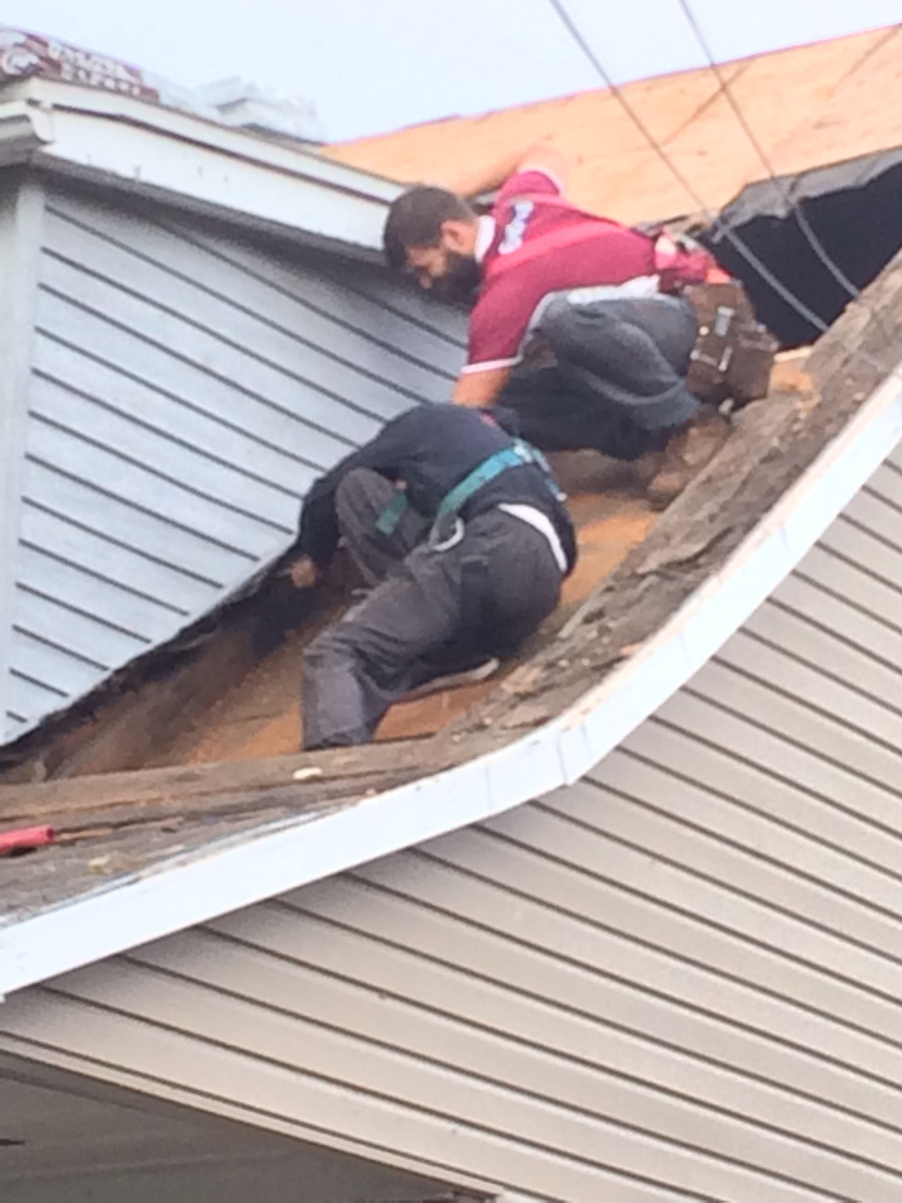 Deux ouvriers réparent le toit pentu d'une maison, l'un en rouge et l'autre en noir, au milieu des bardeaux et du revêtement.
