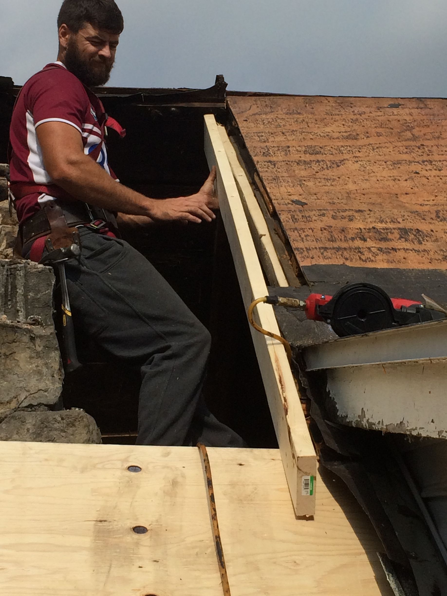 Ouvrier installant une charpente de toit en bois sur un chantier, penché sur une grande planche.
