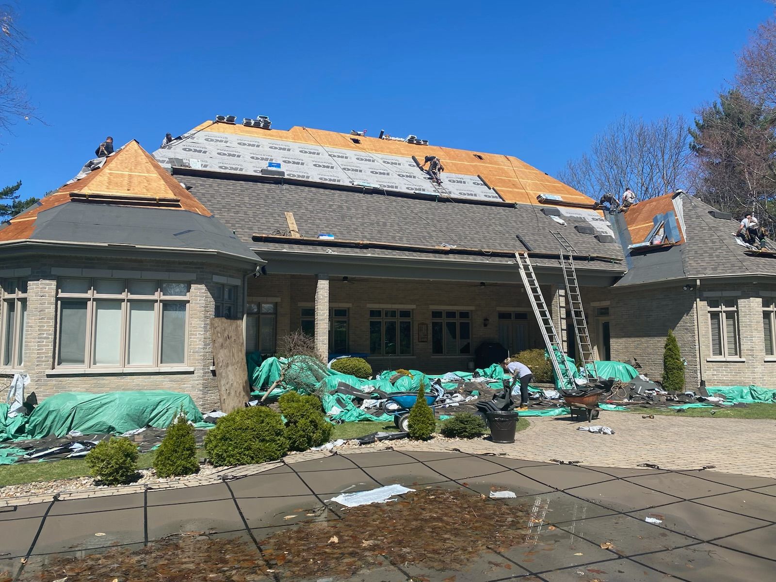 Maison endommagée, toit arraché et débris éparpillés dans la cour avant sous un ciel bleu