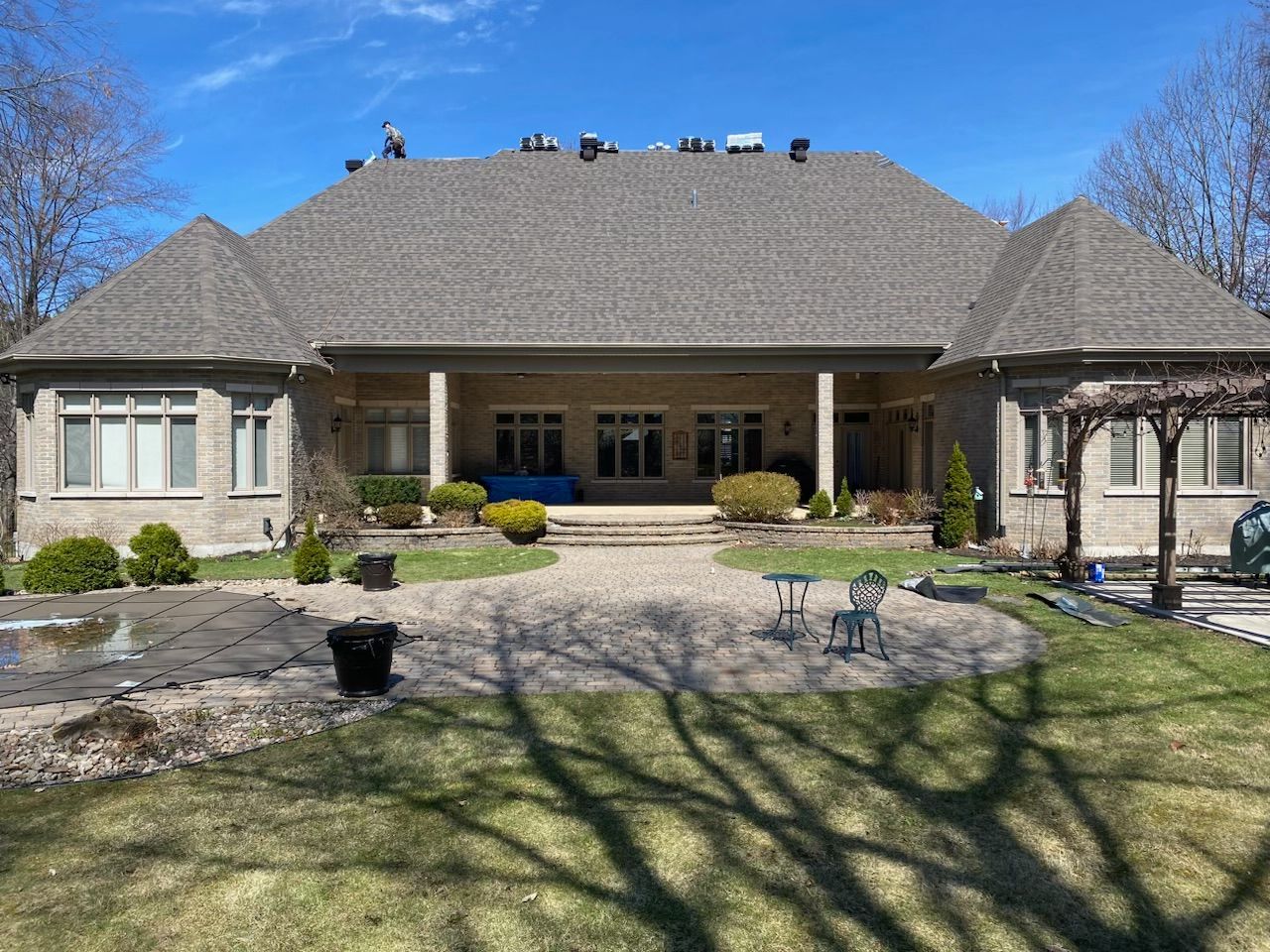 Large beige suburban house with a gray roof, front porch, stone walkway, and lawn under a blue sky