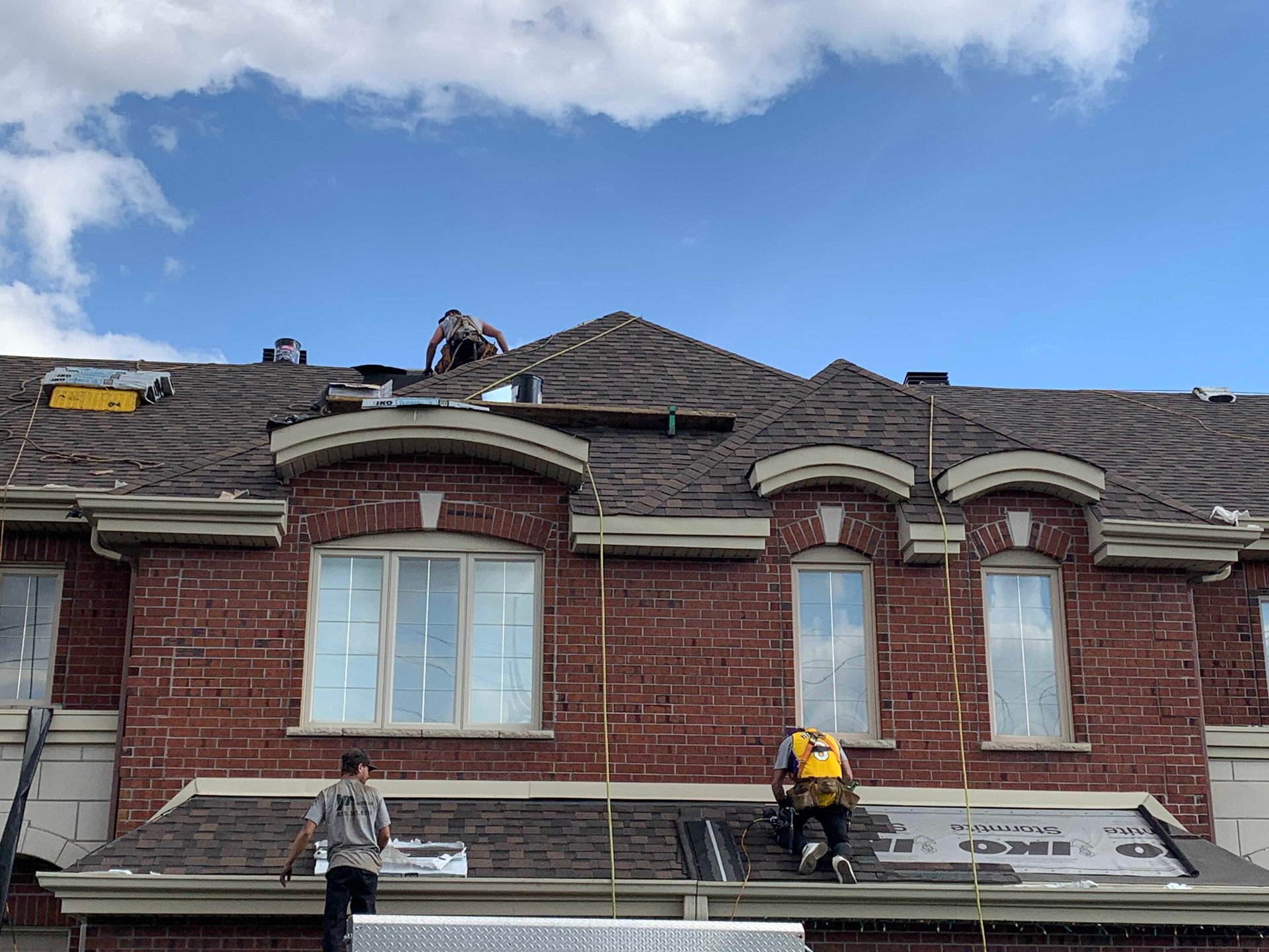 Des ouvriers réparent le toit d'une maison en briques rouges sous un ciel bleu.