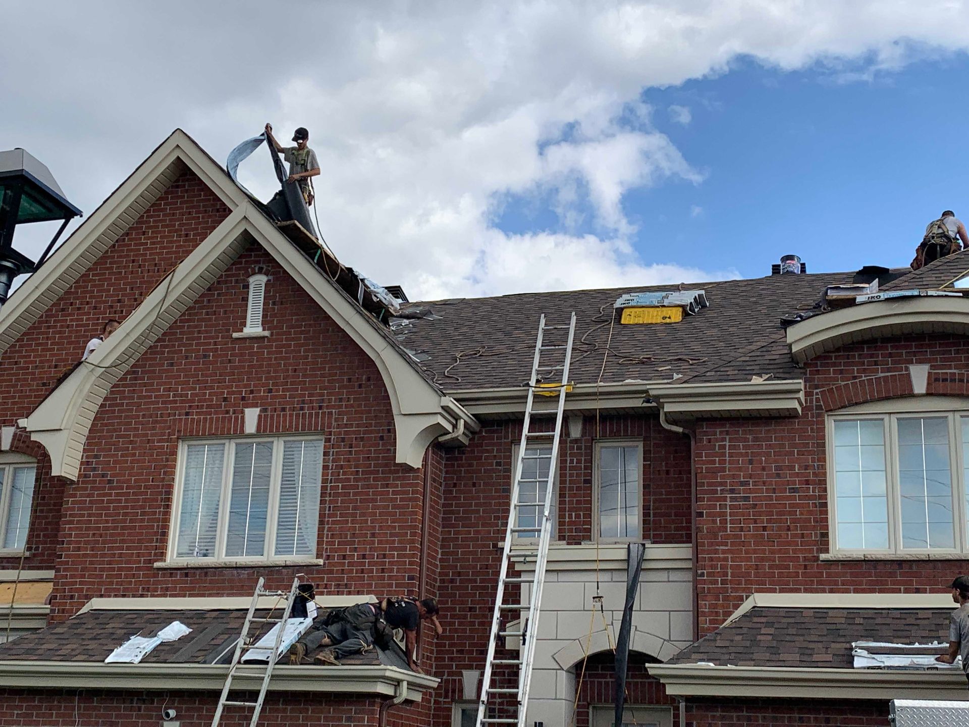 Toiture endommagée d'une maison de ville en briques rouges, avec des ouvriers et des échelles en cours de réparation.