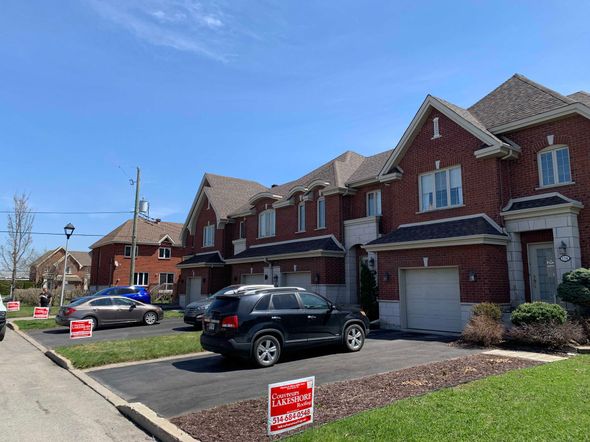 Suburban brick townhouses with parked cars and red real estate signs on a sunny street