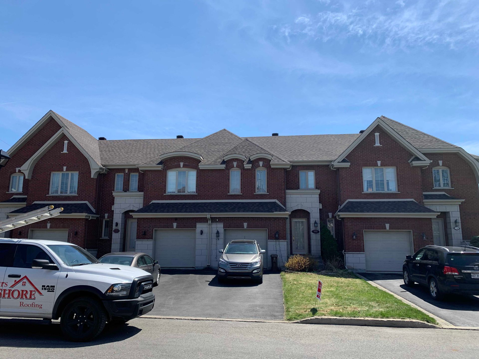 Rangée de maisons de ville en briques avec portes de garage et voitures garées sous un ciel bleu clair