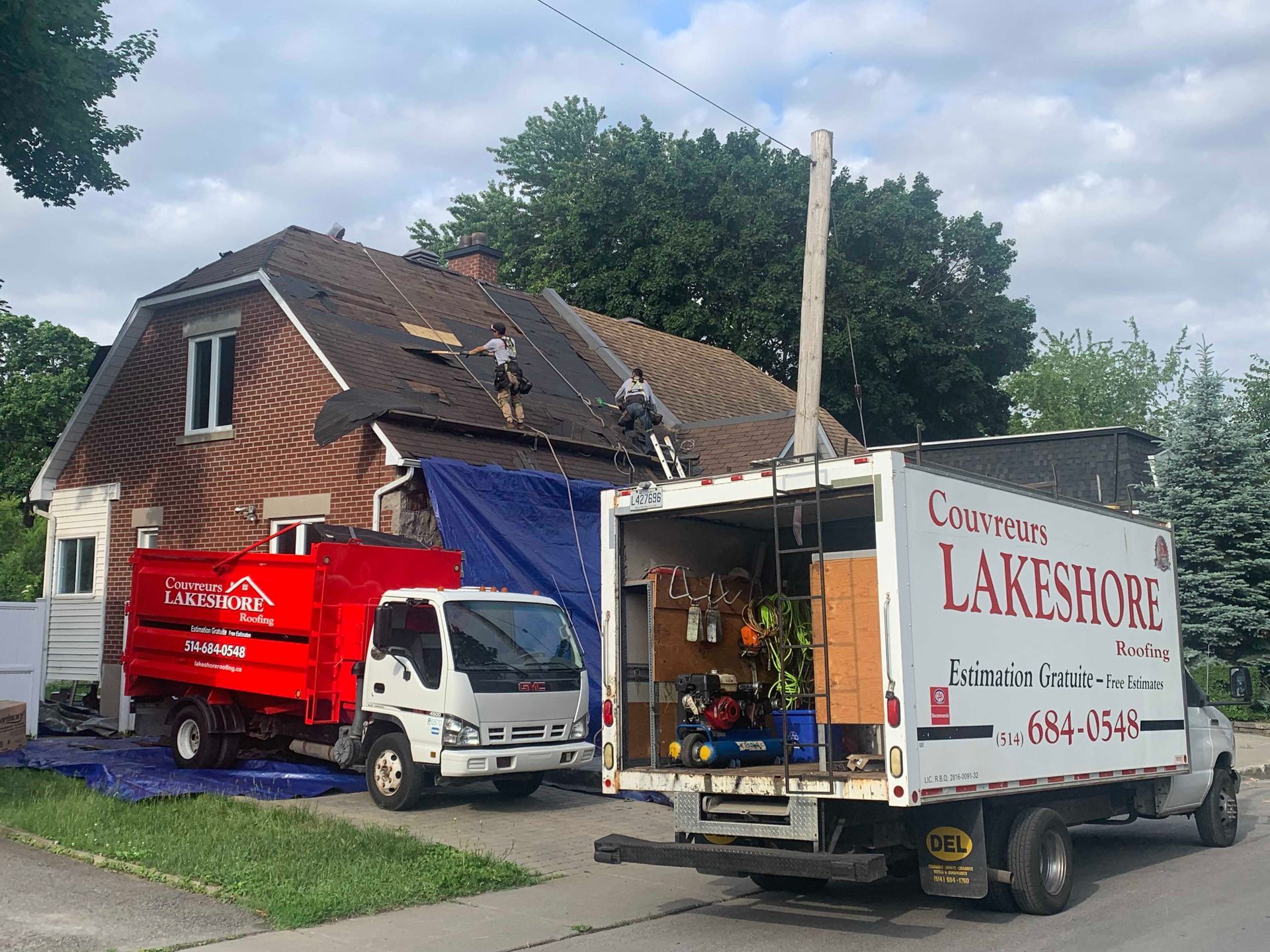 Deux camions de déménagement stationnés près d'une maison ; des ouvriers sur le toit et des cartons de déménagement visibles.