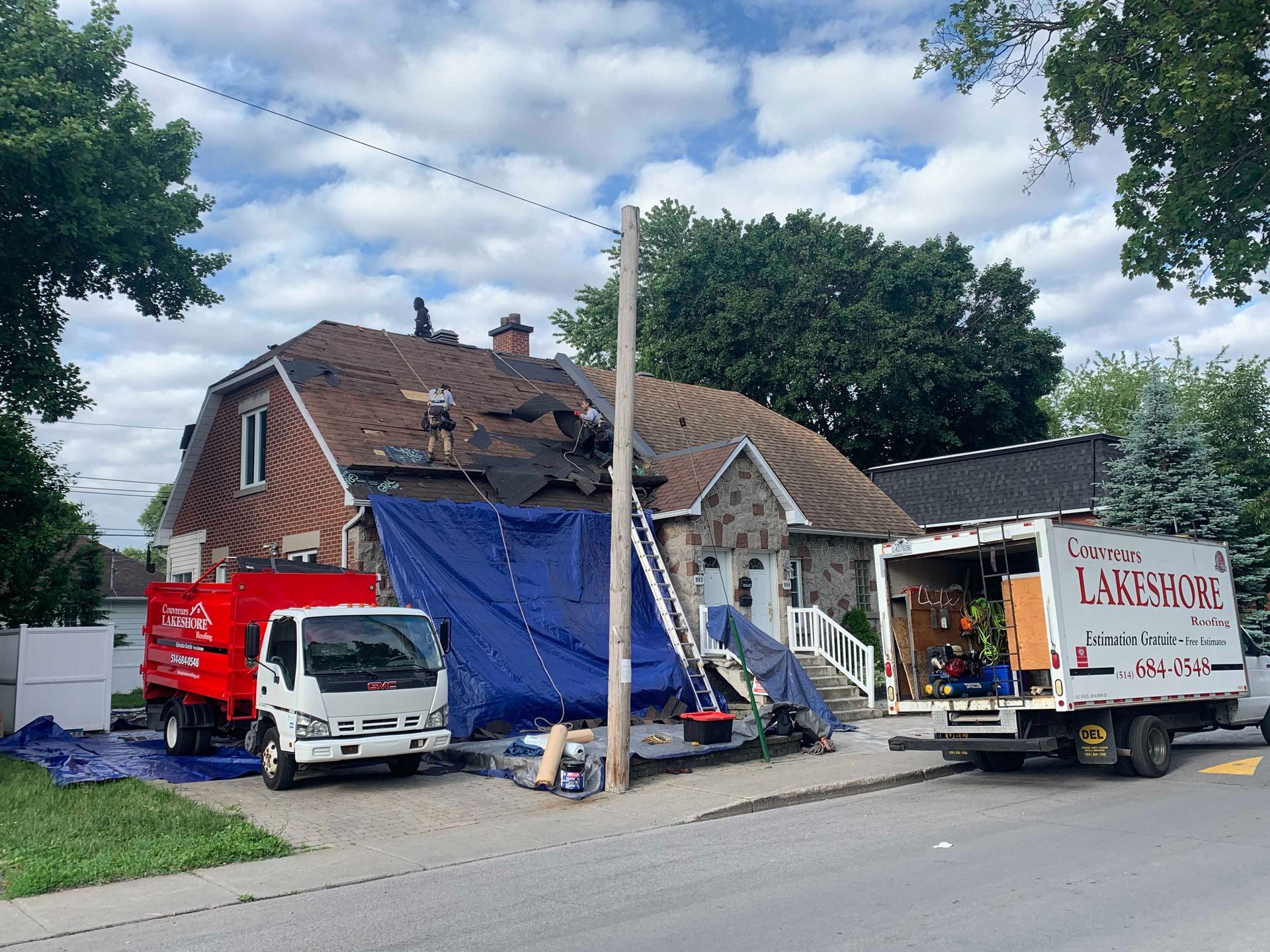 Maison en réparation avec une bâche bleue, camion blanc, fourgonnette rouge et camion de chantier garés dans la rue