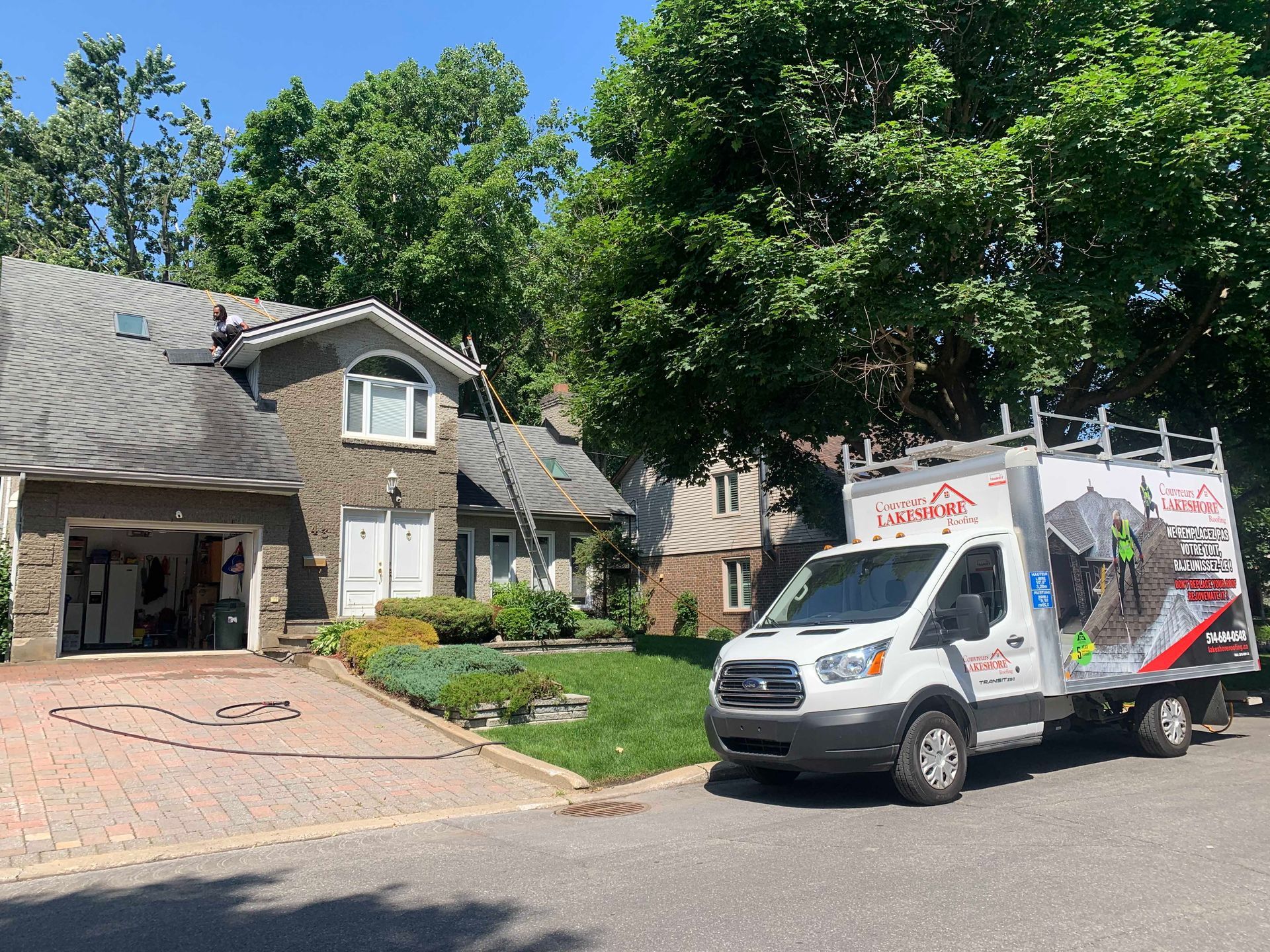 Camion de déménagement stationné devant une maison de banlieue avec garage ouvert et allée en briques.
