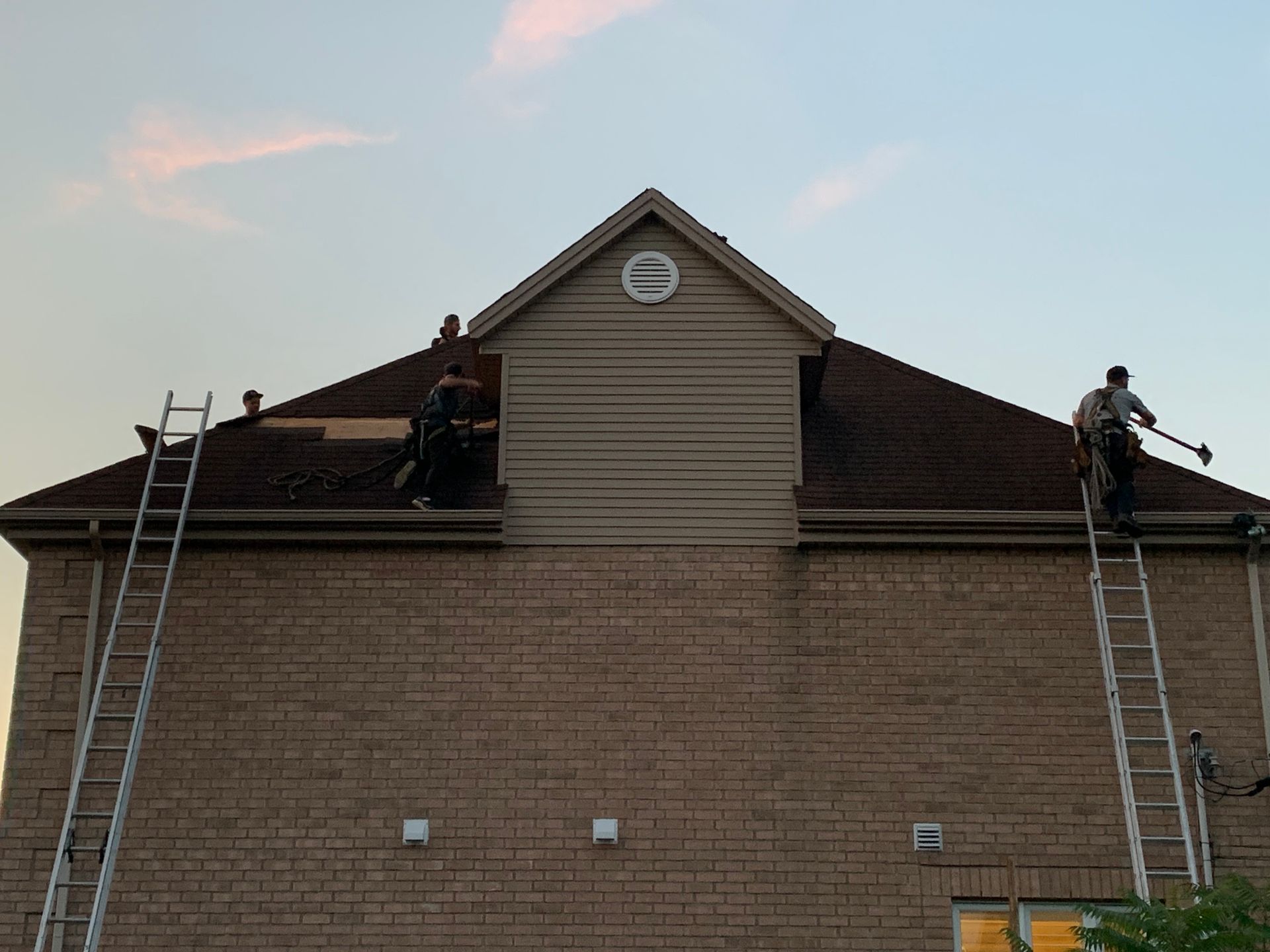 Deux ouvriers sur des échelles réparent le toit d'un bâtiment en briques au crépuscule