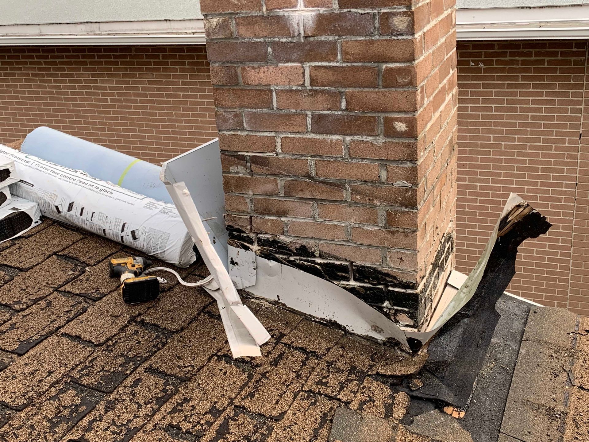 Conduit de ventilation et solins endommagés autour d'une cheminée en briques, avec des débris éparpillés sur les bardeaux.