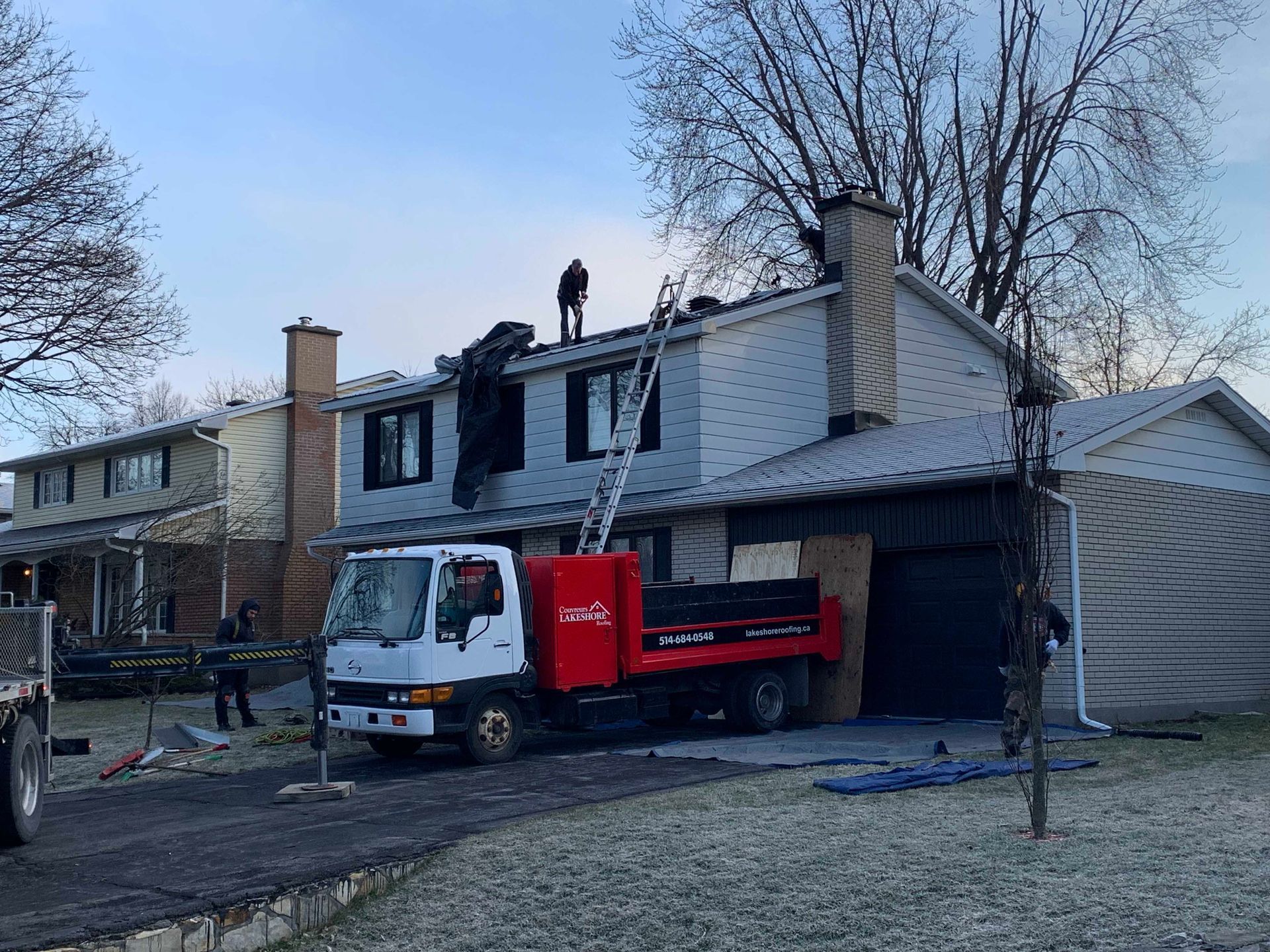 Des ouvriers et un camion utilitaire rouge devant une maison en réparation, une bâche recouvrant le côté droit.