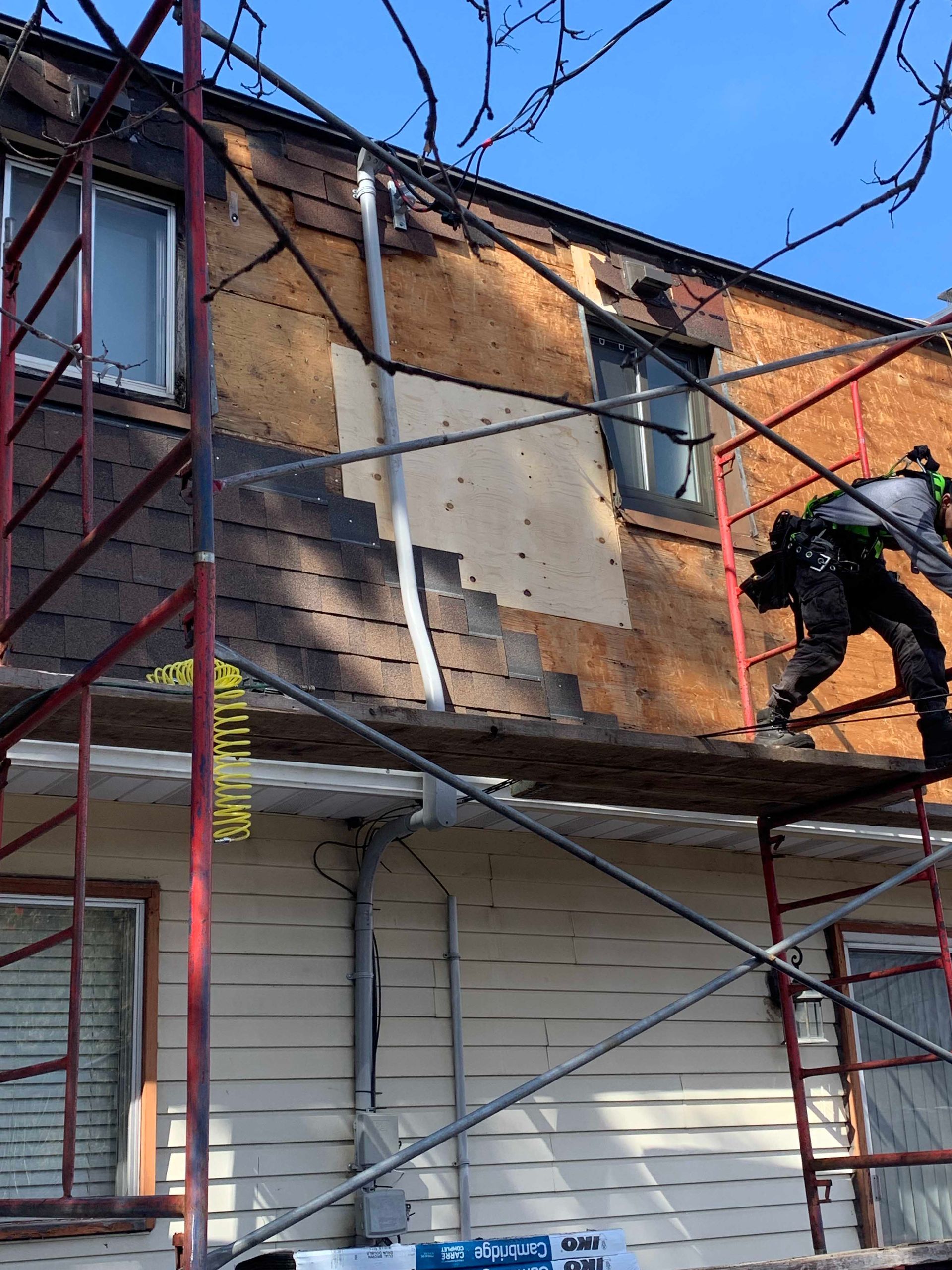 Un ouvrier sur un échafaudage répare le mur extérieur d'une maison sous un ciel bleu.