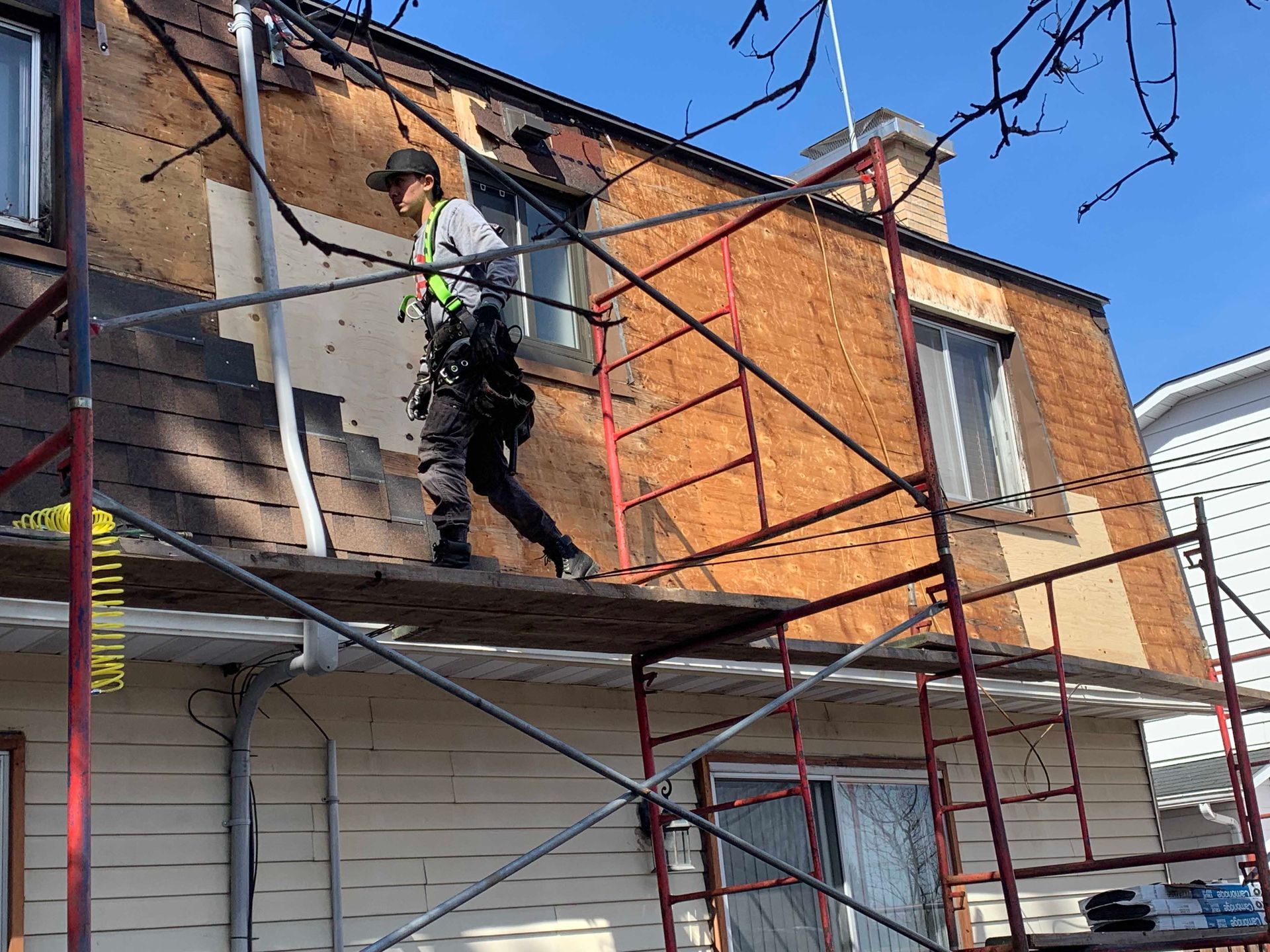 Un ouvrier sur un échafaudage peint la façade d'une maison en briques sous un ciel bleu.