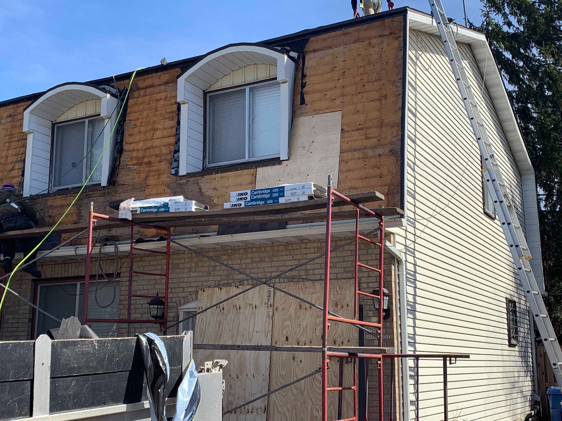 Maison à deux étages en rénovation avec échafaudages rouges et murs extérieurs recouverts de planches