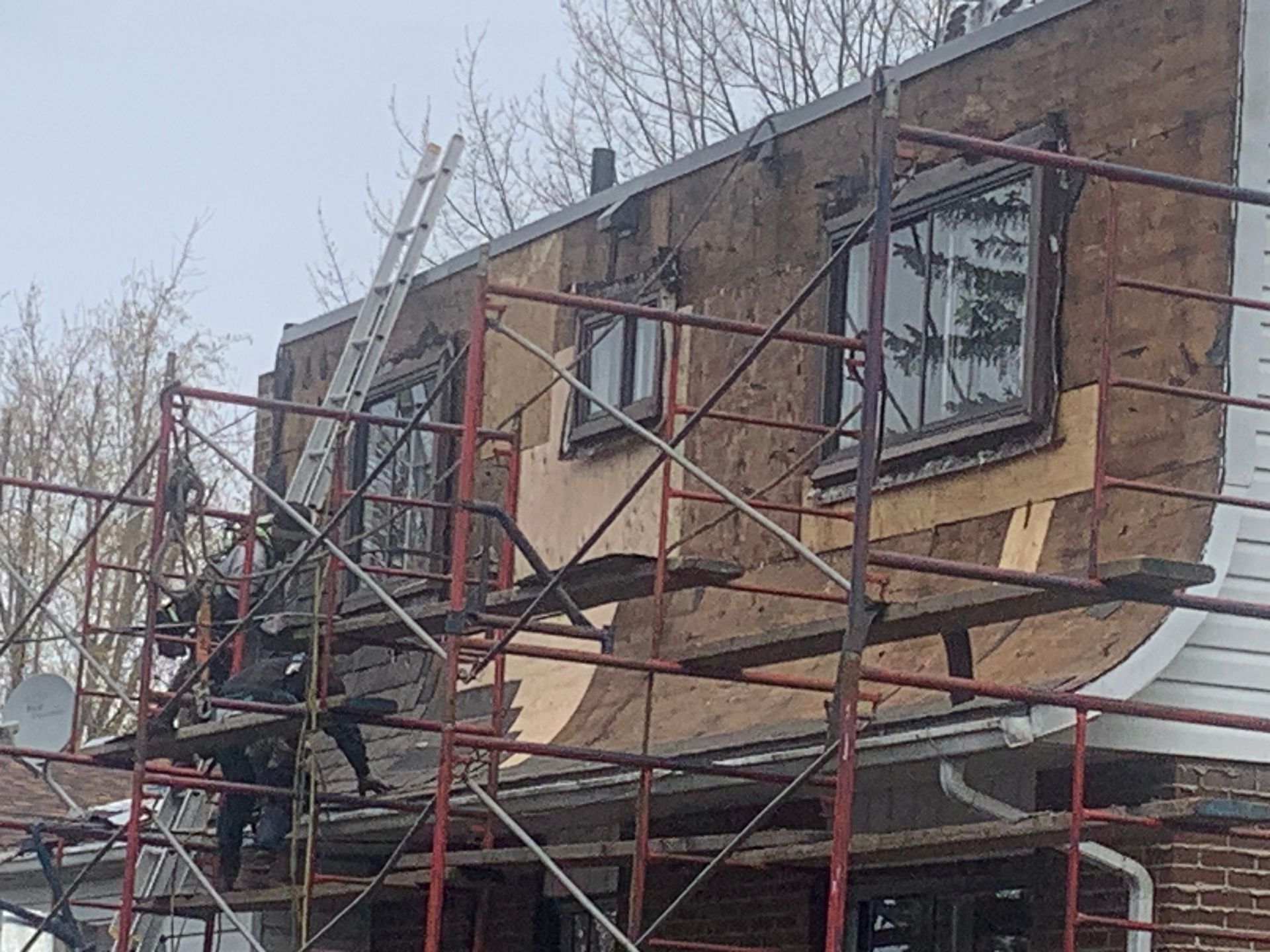 Échafaudages autour d'une maison en briques partiellement rénovée, avec un toit rouge et des fenêtres en construction