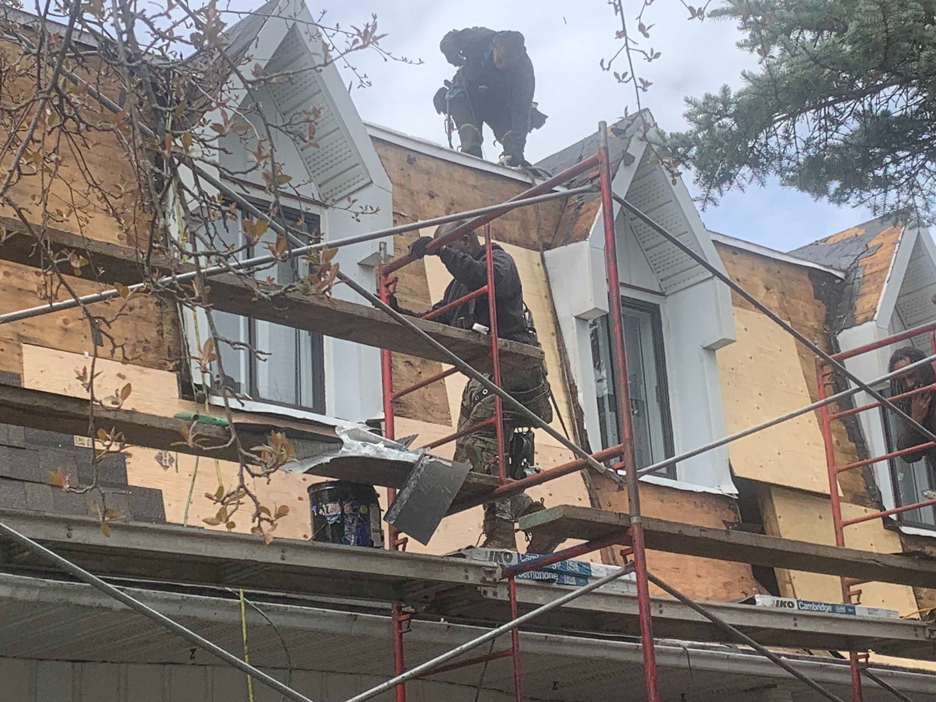 Des ouvriers sur des échafaudages réparent le toit et les fenêtres d'une maison en briques.