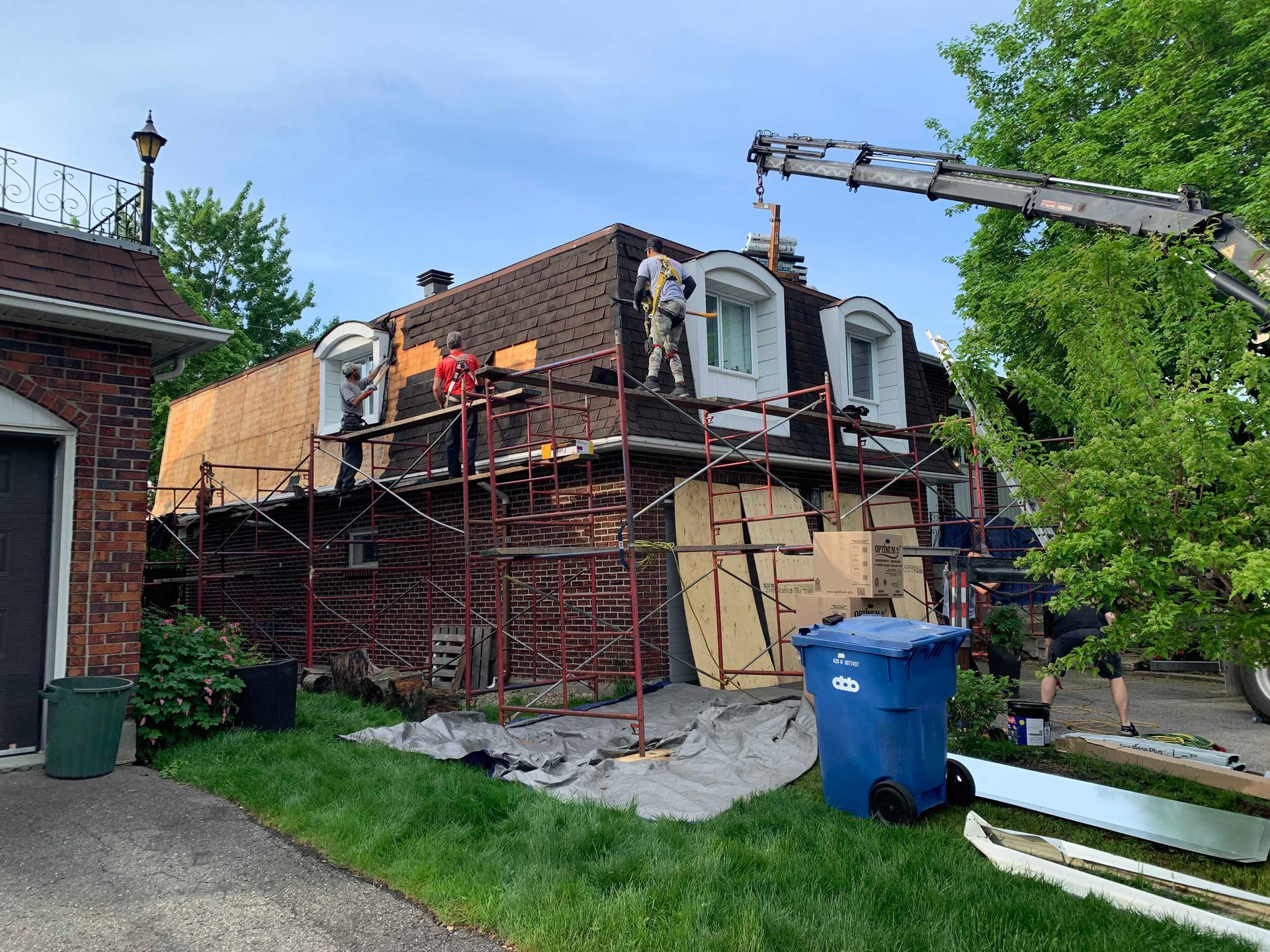 House under renovation with scaffolding, workers, and a blue trash bin in the yard
