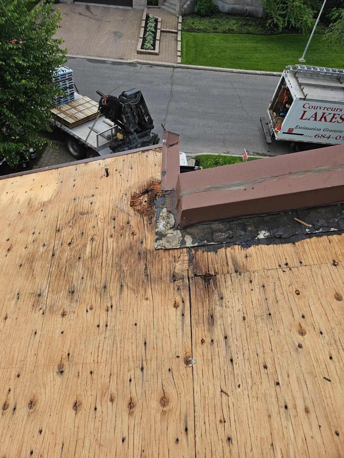 Vue du toit montrant un bord de toit en bois endommagé, avec des matériaux apparents et une rue en contrebas.