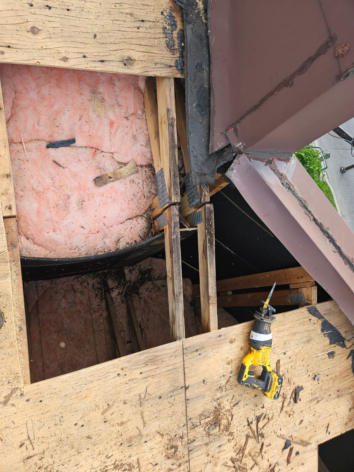 Ouverture de toit en bois endommagée avec isolation rose apparente et perceuse jaune sur une poutre