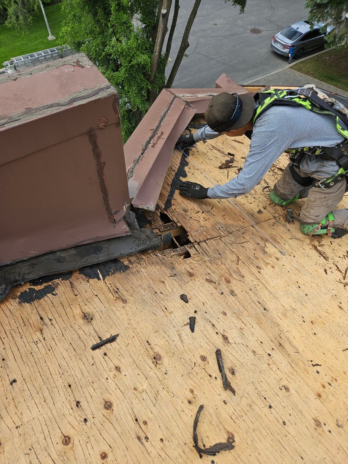 Un ouvrier répare des bardeaux de toiture près d'une cheminée sur un toit à forte pente.