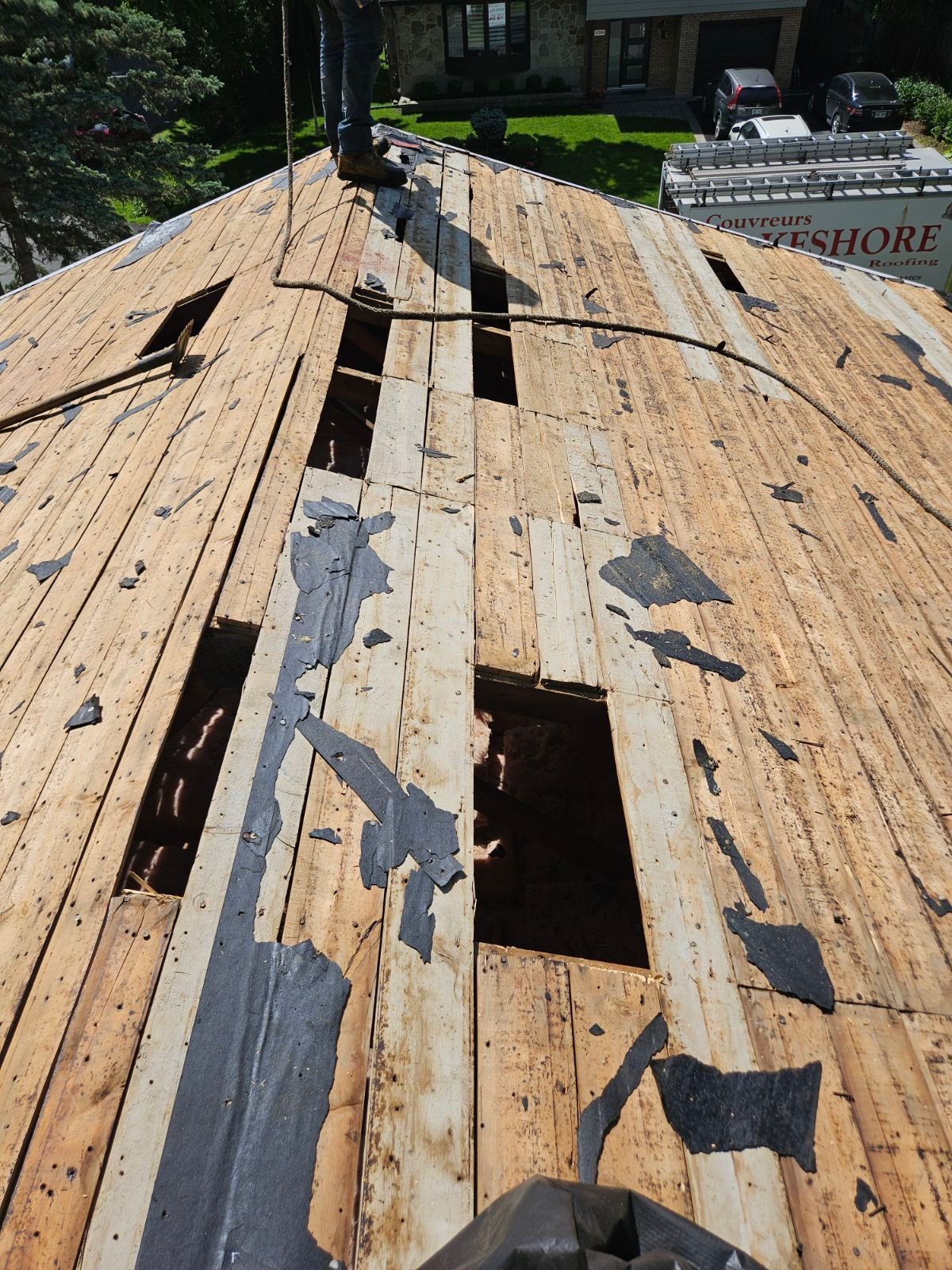 Toiture en bois endommagée, avec des tuiles manquantes et des planches apparentes sous un soleil éclatant